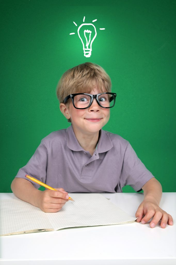 Das Bild zeigt einen kleinen Jungen mit einer großen Brille, der vor einer grünen Tafel sitzt. Auf der Tafel ist eine Glühbirne gezeichnet, und zwar so, dass sie aussieht, als würde sie über dem Kopf des Jungen schweben. In der Lerntherapie geht einem so manches Licht auf