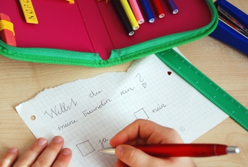 Das Bild zeigt schreibende Kinderhände, die auf einem Zettel den Satz geschrieben haben: Willst Du meine Freundin sein? Ziel der Lerntherapie ist es, dass die Kinder im Alltag normal schreiben können.